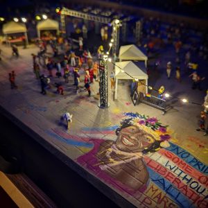An image of a mural painted on the ground. There are people in the distance watching the show on a miniature stage.
