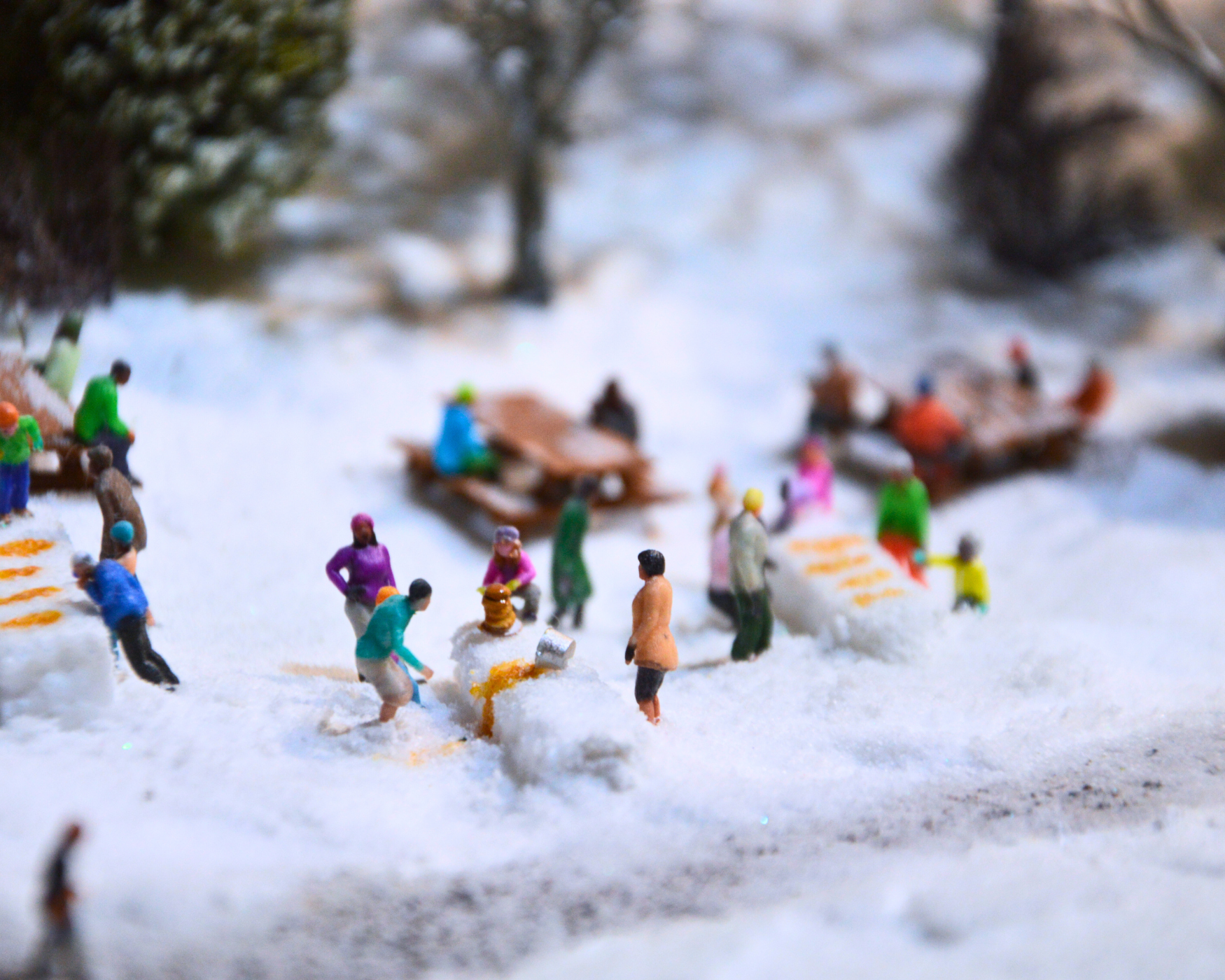 A close up image of a snowy scene with miniature figures sitting at picnic benches.