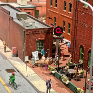 A miniature scene of brown buildings with a person standing on a small stage performing.
