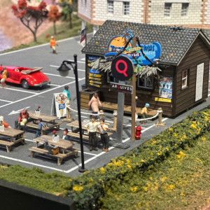 A miniature scene of a small building with picnic tables and two people standing side by side.
