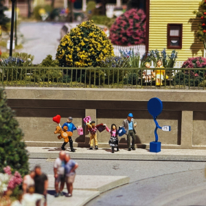 A miniature display of a young girl in a crowd with shopping bags standing next to a miniature blue balloon.