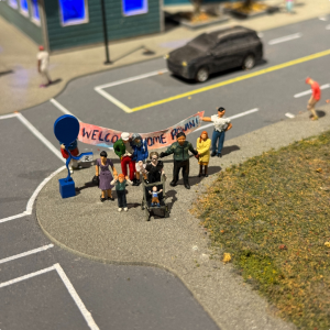 A miniature scene of a crowd holding a sign in front of a young child in a stroller.