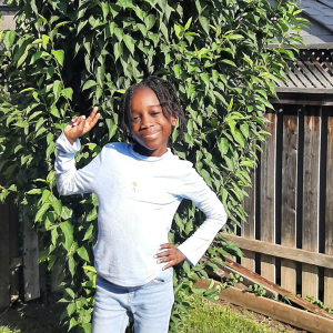 A young person posing for a photo in front of a green bush.