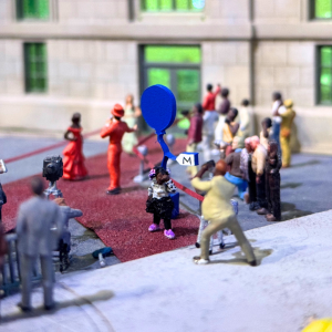 A miniature scene of a young person posing for photos while standing in a crowd.
