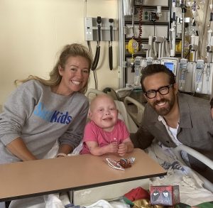 A young person sitting on a hospital bed in between two adults and posing for a photo.