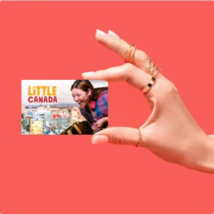A hand holding a gift card with the image of a person looking closely at a miniature display.