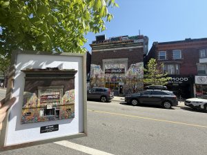 A street view of a building with graffiti and a person holding a miniature facade of the building.